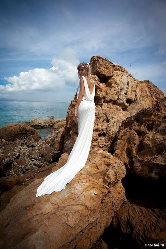 Невеста в белом длинном платье со шлейфом стоит обернувшись на скале  - фото 589790 PhoThai - свадьбы и фотосессии в Таиланде