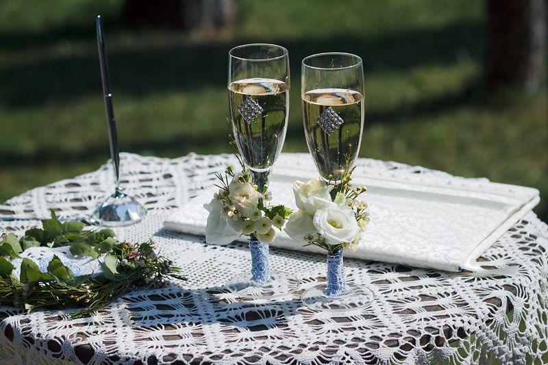 Свадебные бокалы для церемонии, украшенные бутонами белых роз на фоне стола и кружевной салфетки - фото 1496637 Фотограф Ведута Валерий