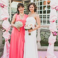 Невеста в длинном открытом белом платье А-образного силуэта и подружка в розовом длинном приталенном поясом платье с  V-образным вырезом держат букеты под аркой декорированной розовой тканью и цветами