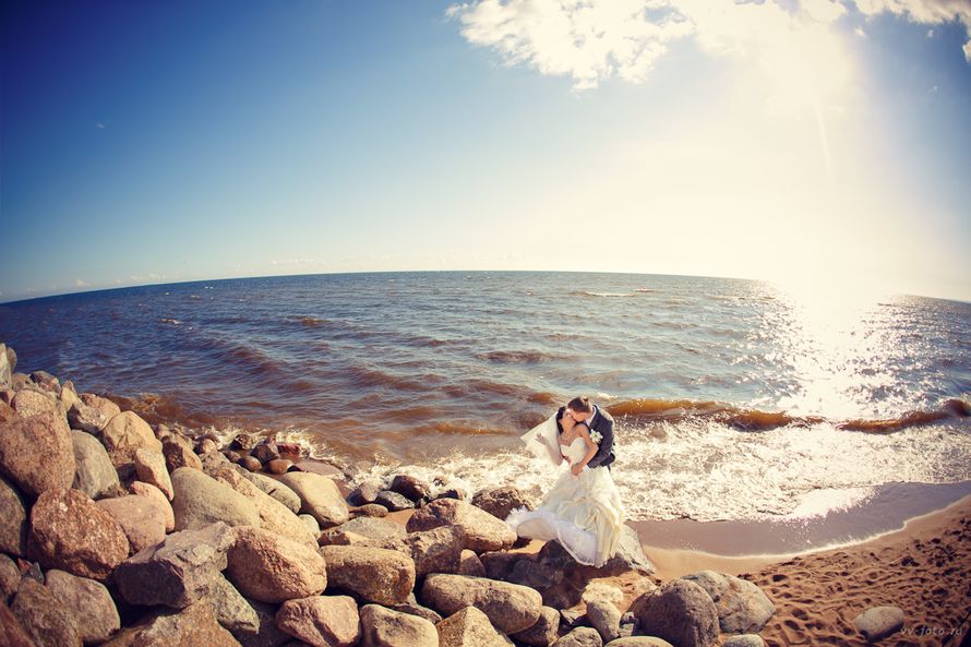 На пляже, стоят обнявшись и целуясь, жених и невеста, она в белом, длинном платье с фатой, он в черном жилете и брюках - фото 1631799 Фотограф Валерий Васильев