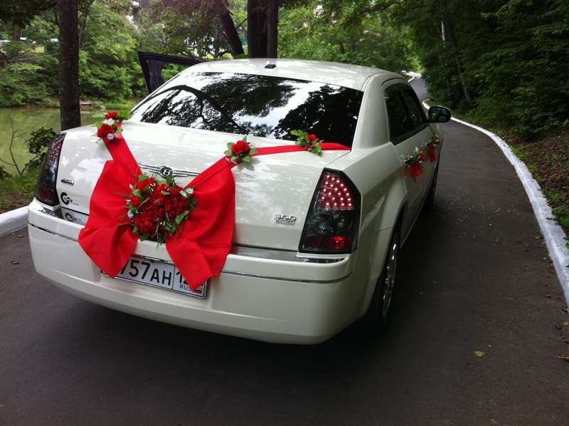 Шикарный красный большой бант, в сердцевине которого экибана из красных роз украшает багажник белого автомобиля. - фото 698517 RentVIPauto - аренда авто на свадьбу