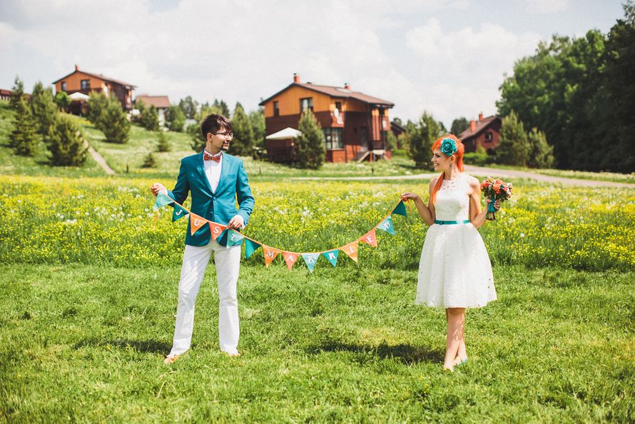Жених и невеста на фоне поля и деревянных домов держат бумажную гирлянду  - фото 3332955 Фотограф Екатерина Огарская
