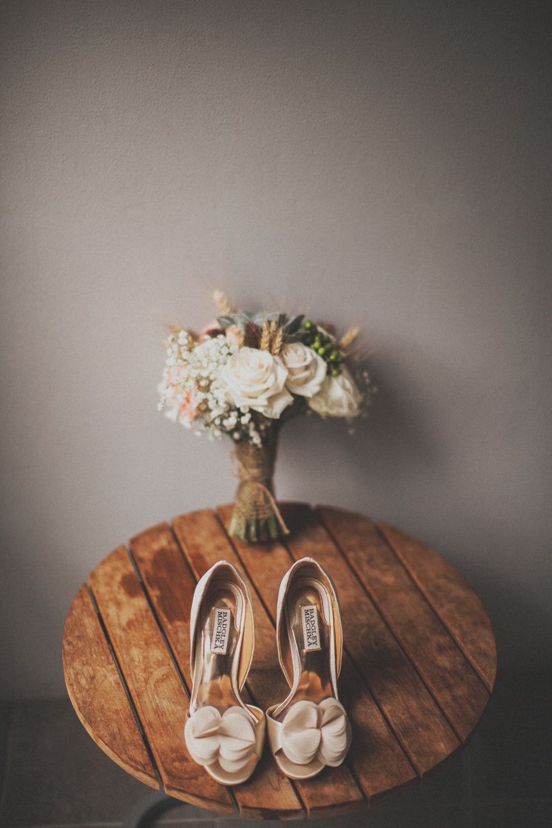 Бежевые туфли на высоком каблуке украшенными декоративным цветком стоят на деревянном столе возле букета. - фото 1731175 Wedding and event studio Leto