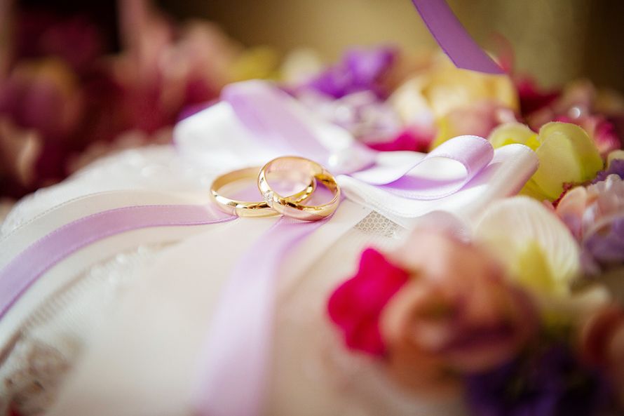 Золотые обручальные кольца, выполнены в классическом стиле   на фоне белой ткани, сиреневых лент и лепестков. - фото 2774127 Праздничное агентство "Пион"