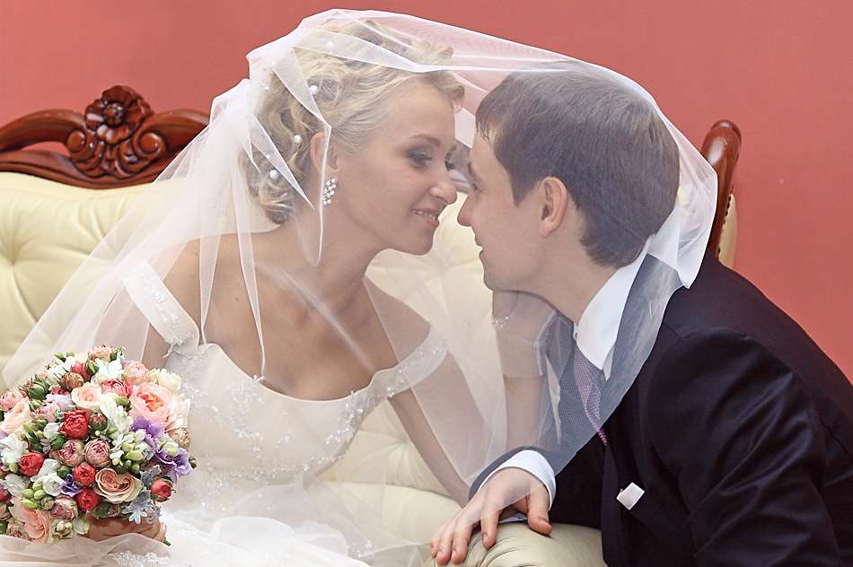 Невеста улыбается жениху накинув на него фату на диване в Грибоедовском загсе - фото 2062722 Marryday - свадебная фотография