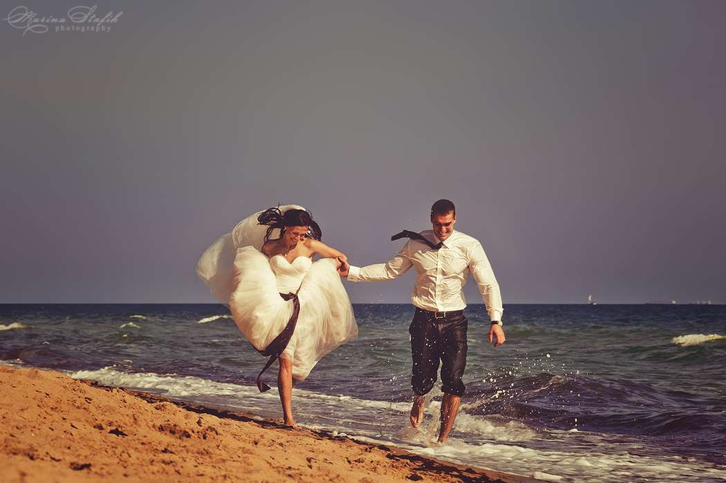Невеста и жених бегут босиком по краю моря, держась за руки, он в черных брюках и белой рубашке с галстуком, она в белом  летящем - фото 2151034 Photographer Marina Stafik