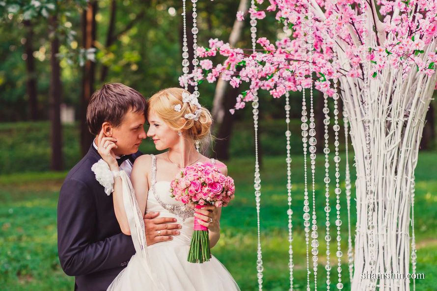 Возле дерева, цветущего розовыми цветами и украшенного стеклянными гирляндами, стоят жених и невеста  - фото 2333250 Видео-фото студия Гранд