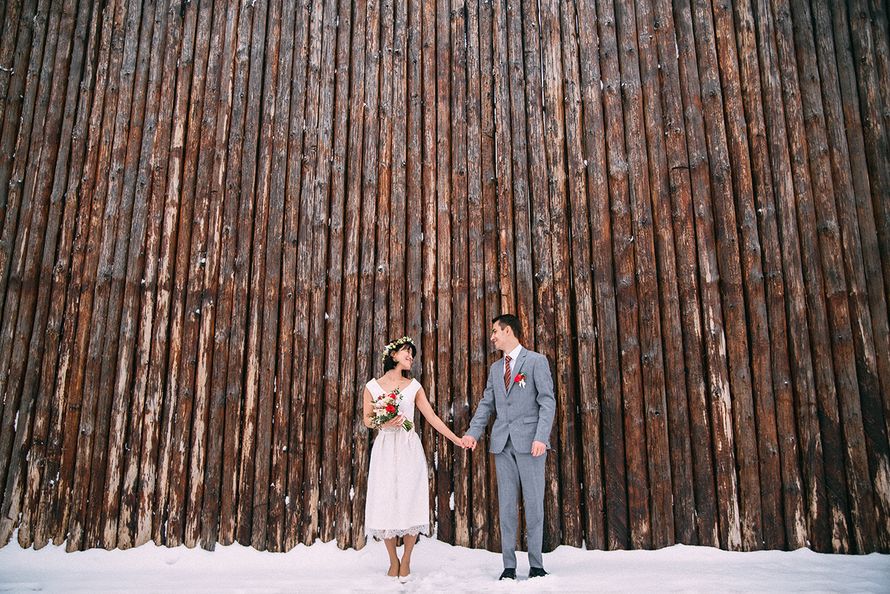 Жених и невеста, держась за руки, стоят  на фоне деревянного ограждения на снегу - фото 3569019 Фотограф Олег Онищук