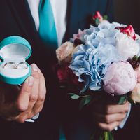 Жених с букетом невесты из гортензий, роз, пионов и рубуса и обручальными кольцами 