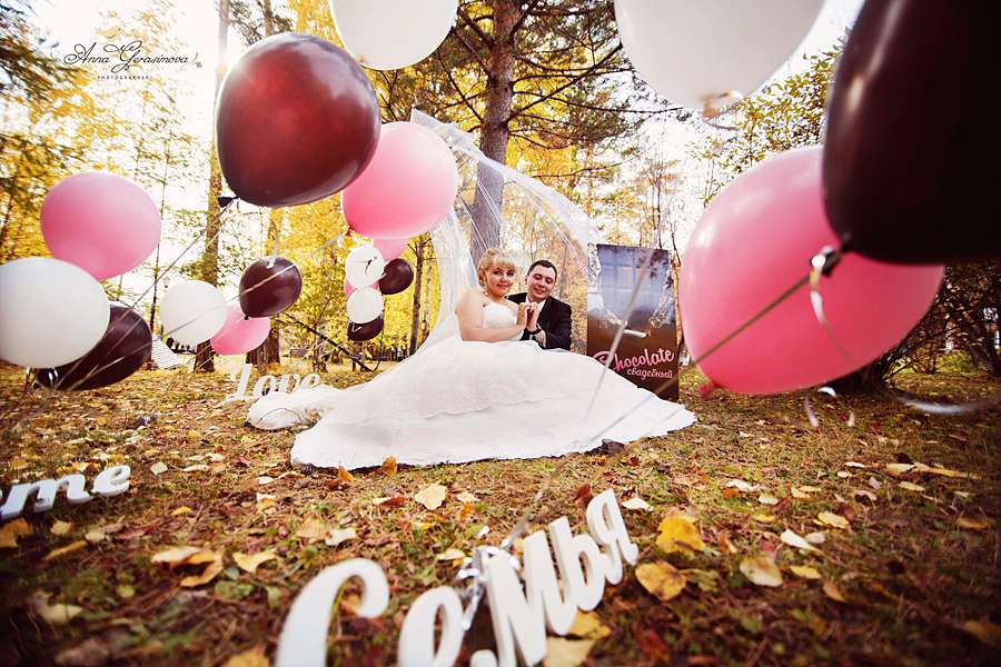 На осенней листве возле дерева между розовыми и коричневыми шарами сидят жених и невеста - фото 3208383 Свадебный фотограф Анна Герасимова