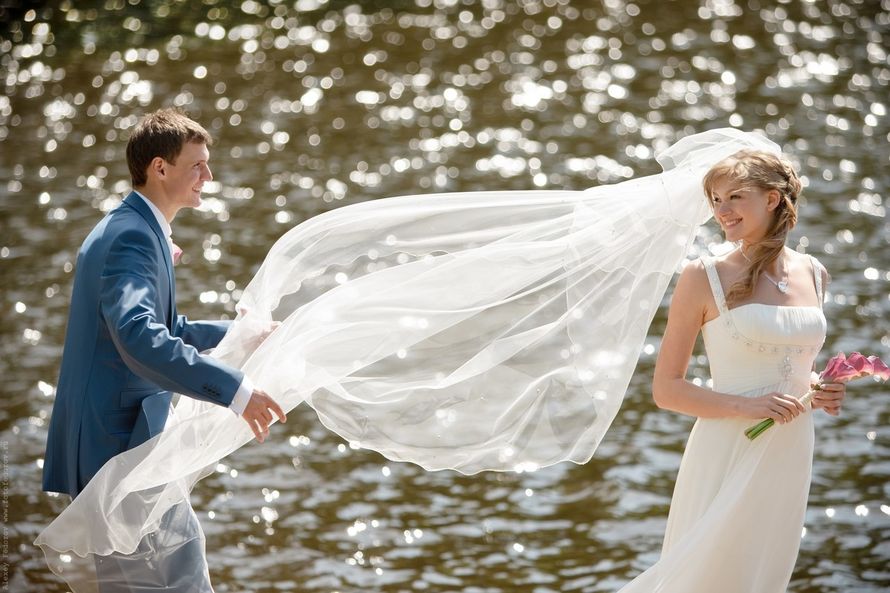 Жених поправляет фату невесты  на фоне водоема - фото 3373043 Fotkay.ru