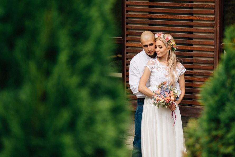 Жених и невеста, прислонившись друг к другу, стоят на фоне зелени и деревянного дома - фото 3525543 Фотография Klenkovphoto