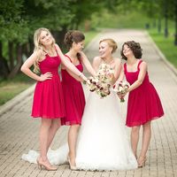 Невеста в длинном платье со шлейфом и подружки с букетиками в красных платьях миди на широких бретельках, расклешенным низом и бежевых туфельках  на парковой аллее
