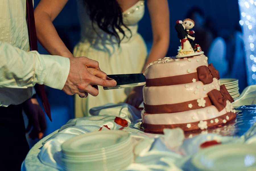 Жених с невестой, разрезающие  
свадебный торт, украшенный коричневыми бантиками, белыми сахарными цветами и фигуркой молодых - фото 516604 Your marusia (Маша)