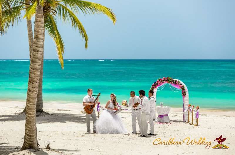 На тропическом пляже танцует невеста в белоснежном платье, жених в белых брюках и рубашке играет на гитаре, рядом аплодируют - фото 2561181 Caribbean Wedding - свадьба в Доминикане