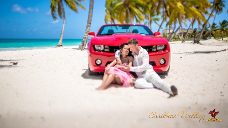 На тропическом пляже перед красным кабриолетом сидят влюбленные, парень в белом летнем костюме обнимает за плечи девушку в - фото 2714109 Caribbean Wedding - свадьба в Доминикане